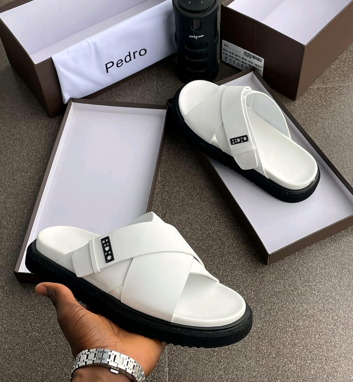 White Pedro crisscross slides with black platform sole shown in box and held by hand