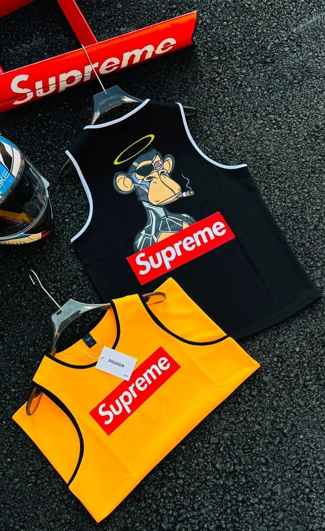 Yellow Supreme box logo armless tank top shown alongside black version on dark textured ground with accessories.