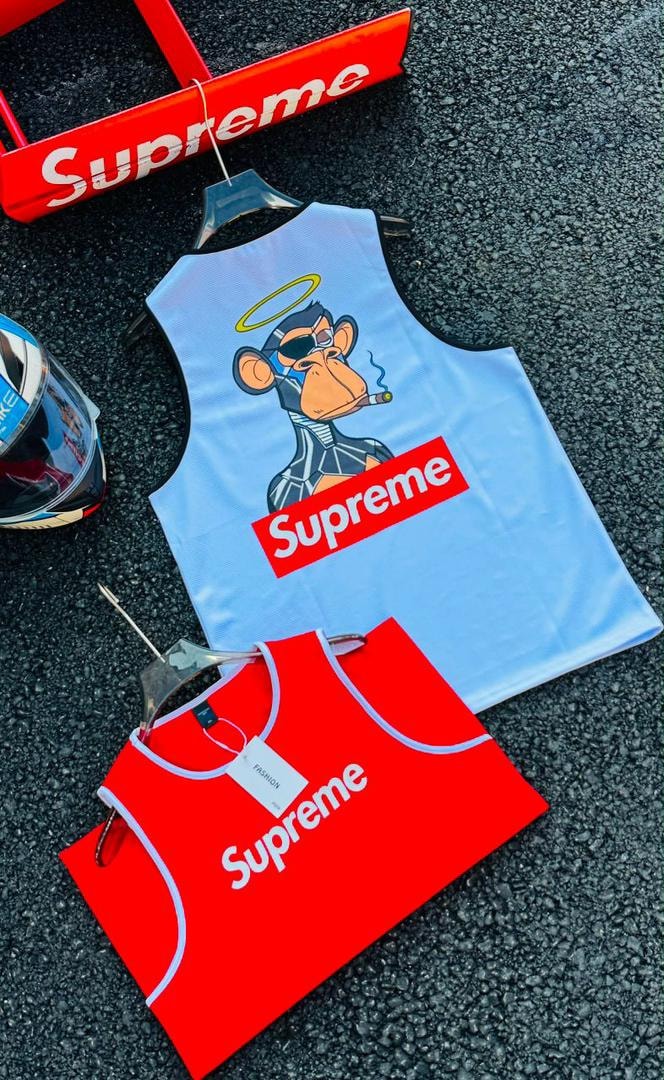 Light blue Supreme monkey graphic armless tank top displayed on dark asphalt with red version, helmet and Supreme sign.