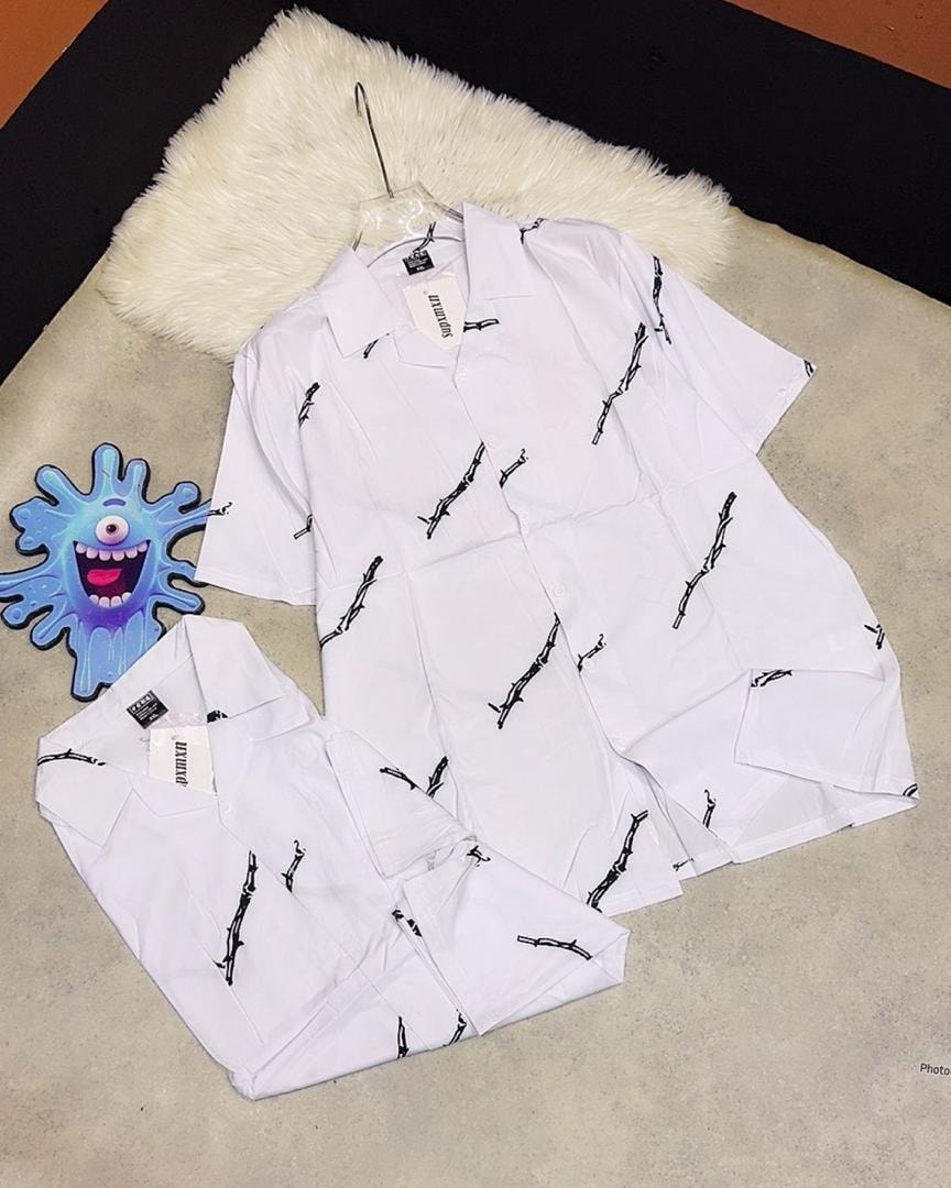 White short sleeve shirt with black abstract branch patterns on hanger and laid flat.