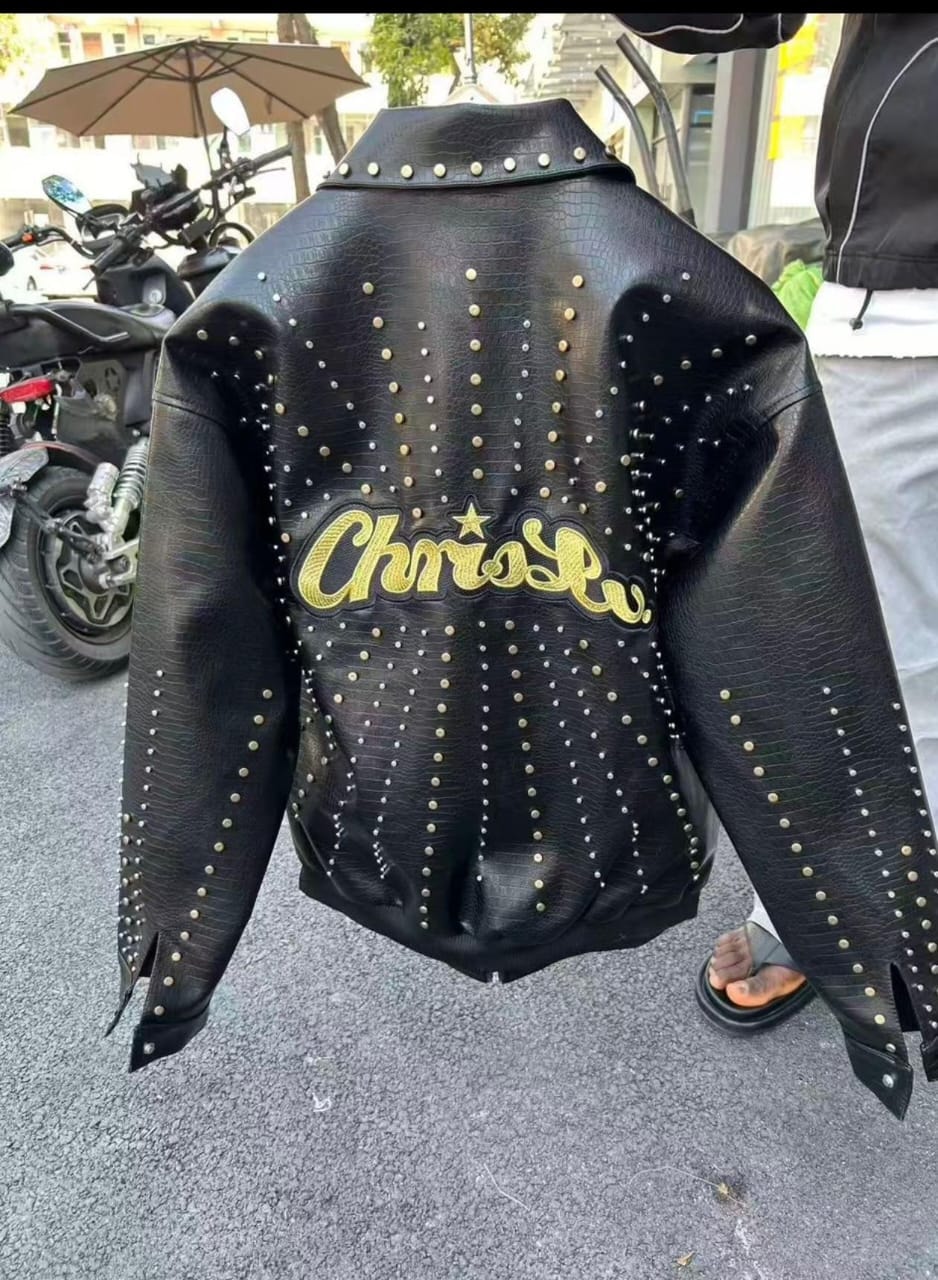 Back view of black studded leather jacket with yellow ChrisRo star embroidery held outdoors.