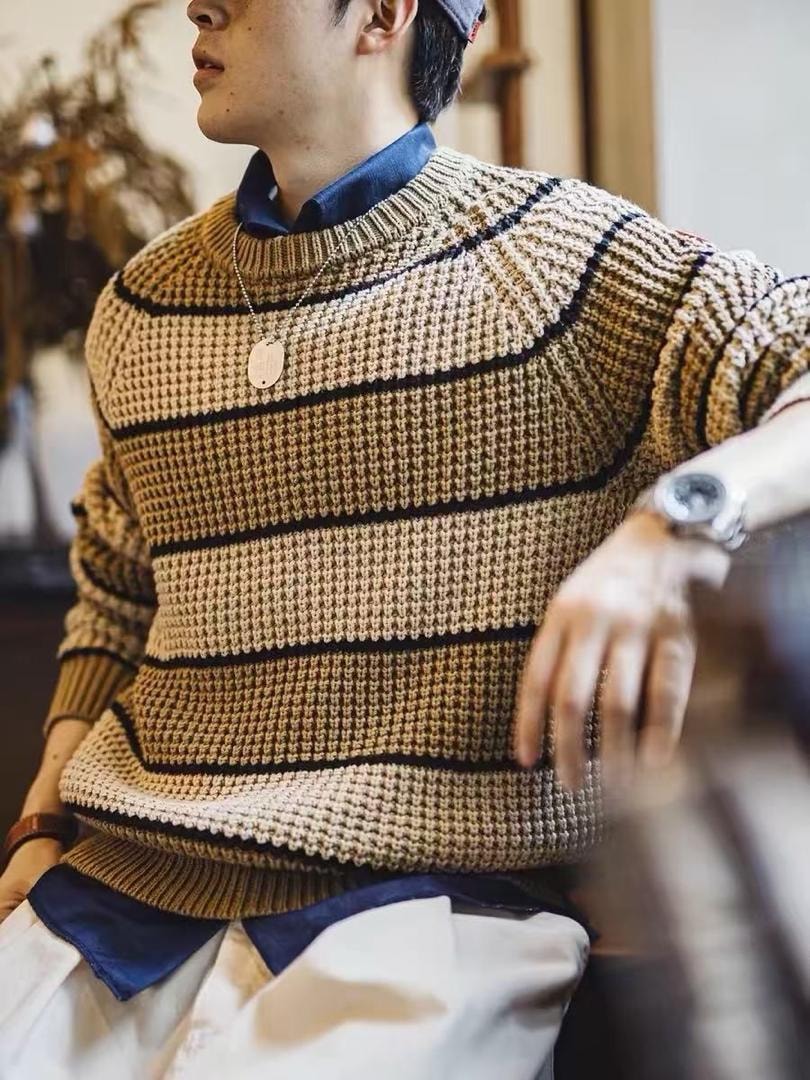 Man modeling beige striped knitted sweater with layered shirt and accessories.