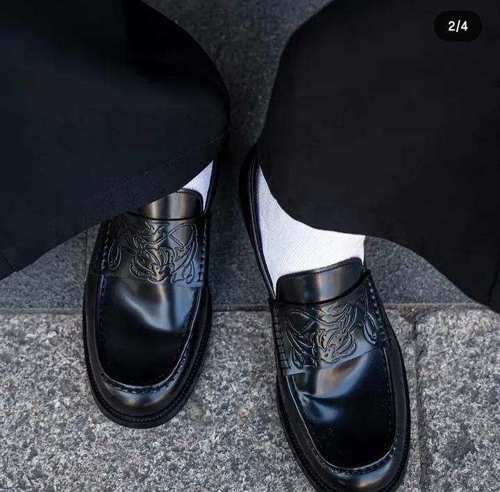 Black embossed loafers worn with black trousers on paved surface.