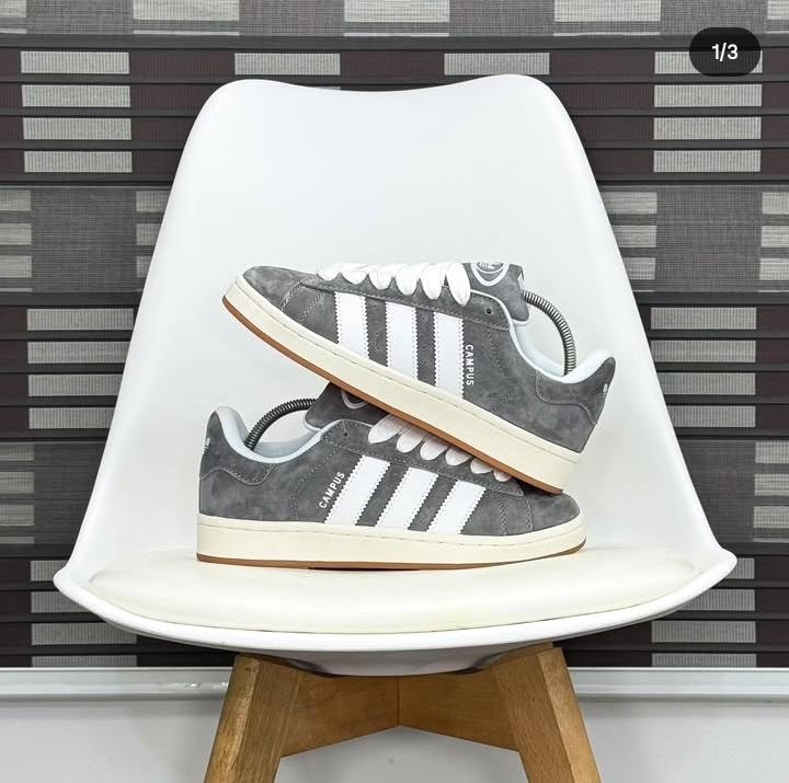 Gray Adidas Campus sneakers with white stripes displayed on white chair.