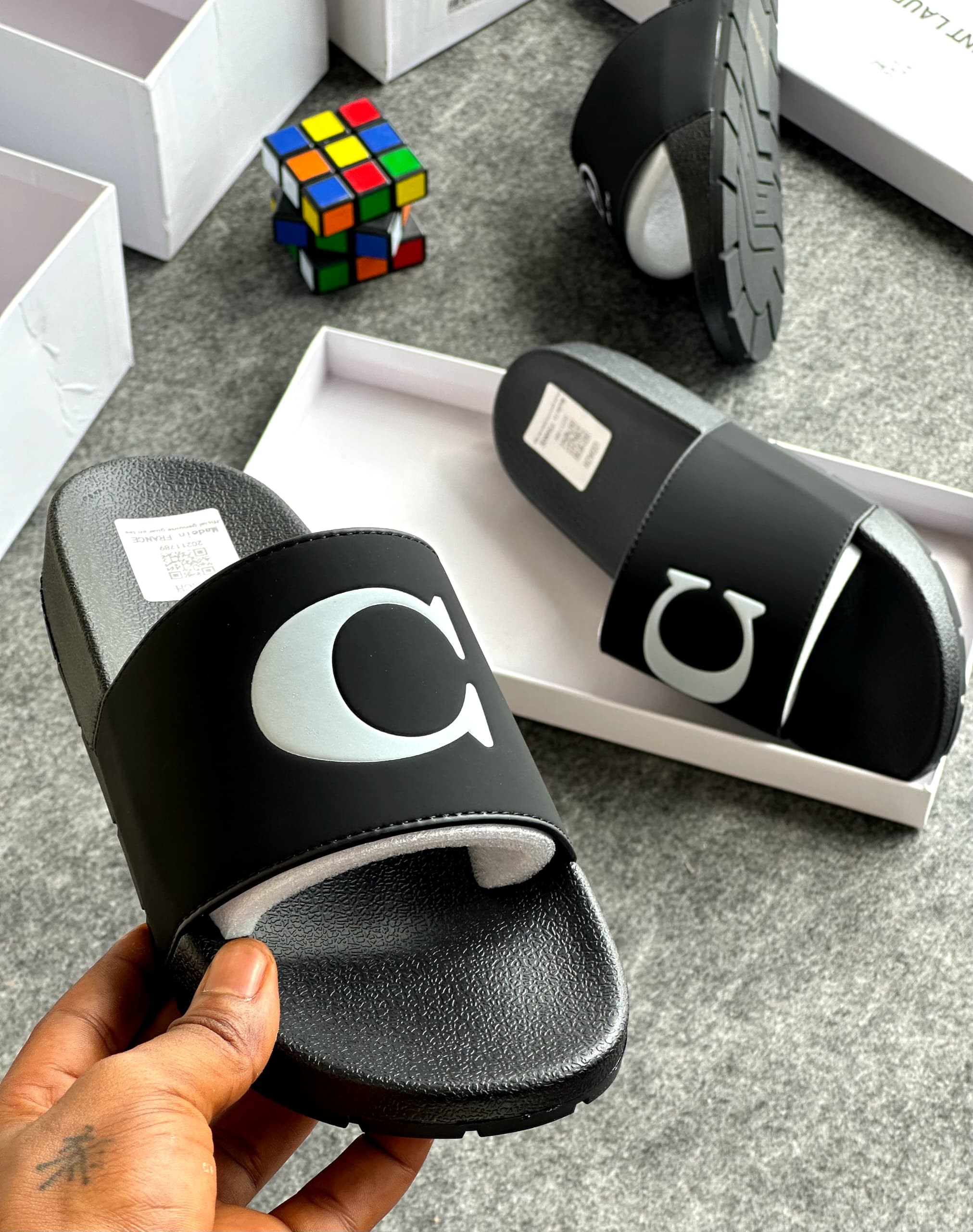 Black slide with large white C logo held in hand with packaging and Rubik's cube visible.
