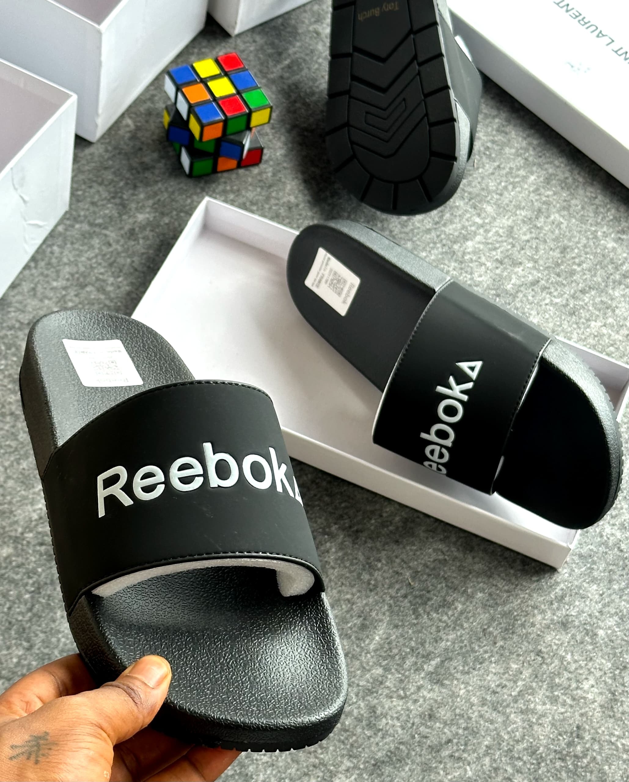 Black Reebok slide with white logo held showing the branding and background.
