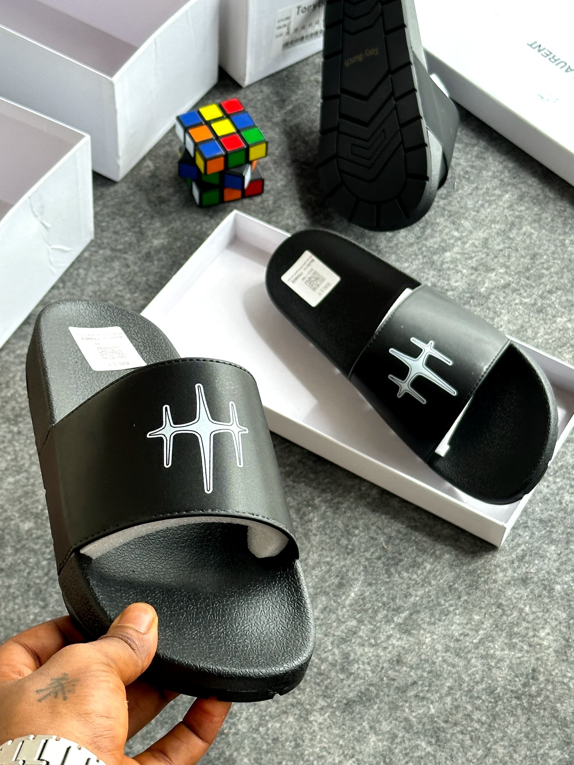 Black slide with white star-like logo on strap, shown in hand with background details.