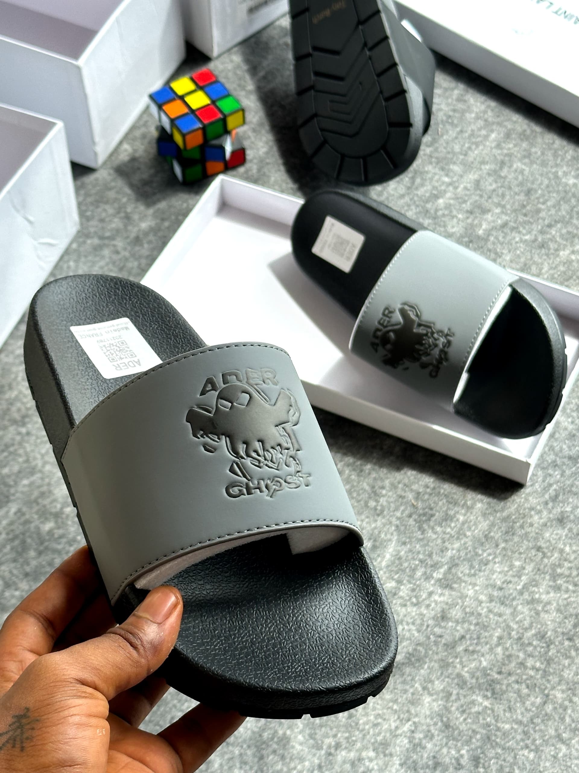 Gray and black Ader Error Ghost slide with skull graphic held in hand showing branding.