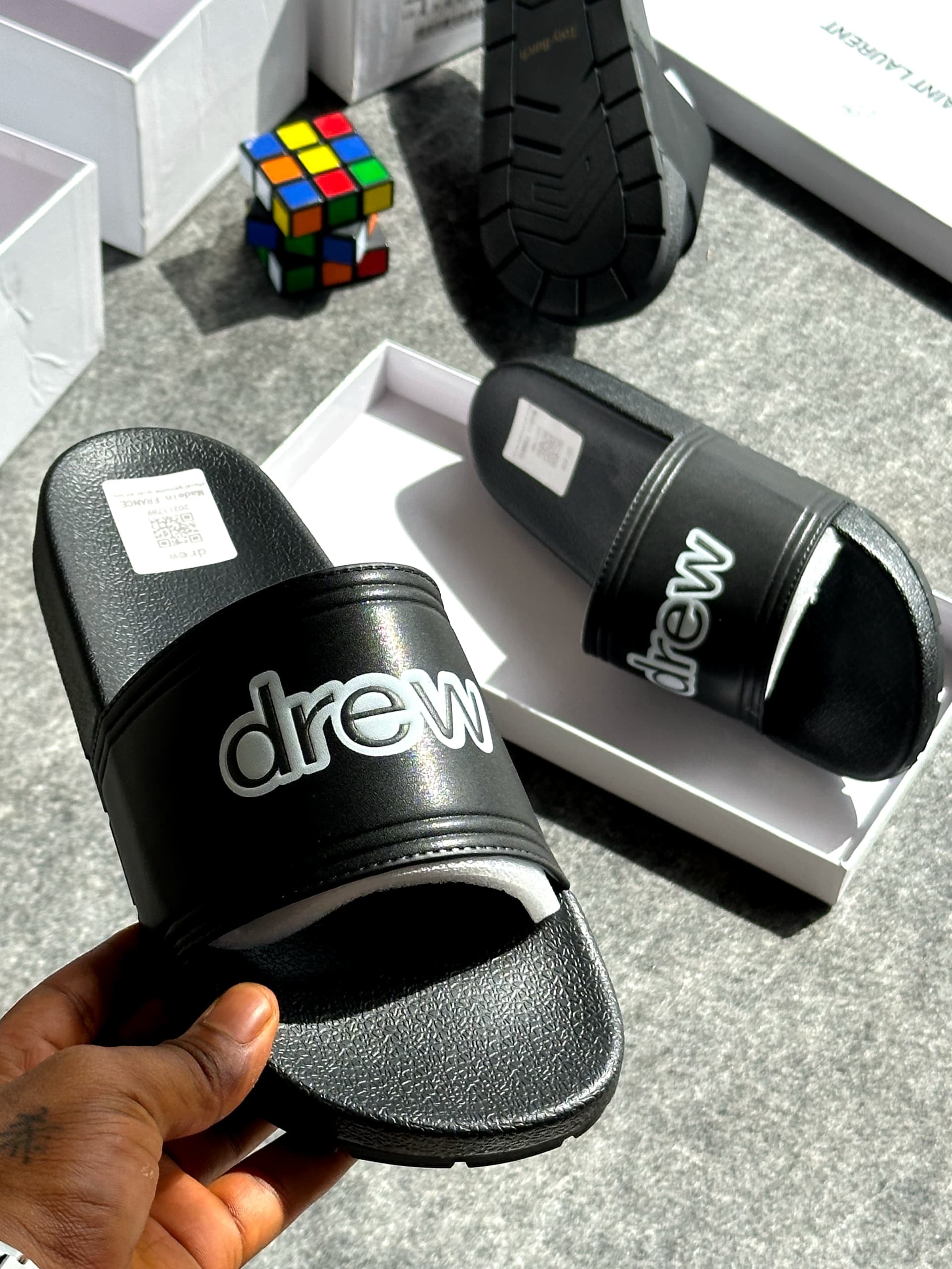 Black slide with drew logo in white, shown held with packaging and colorful cube in background.