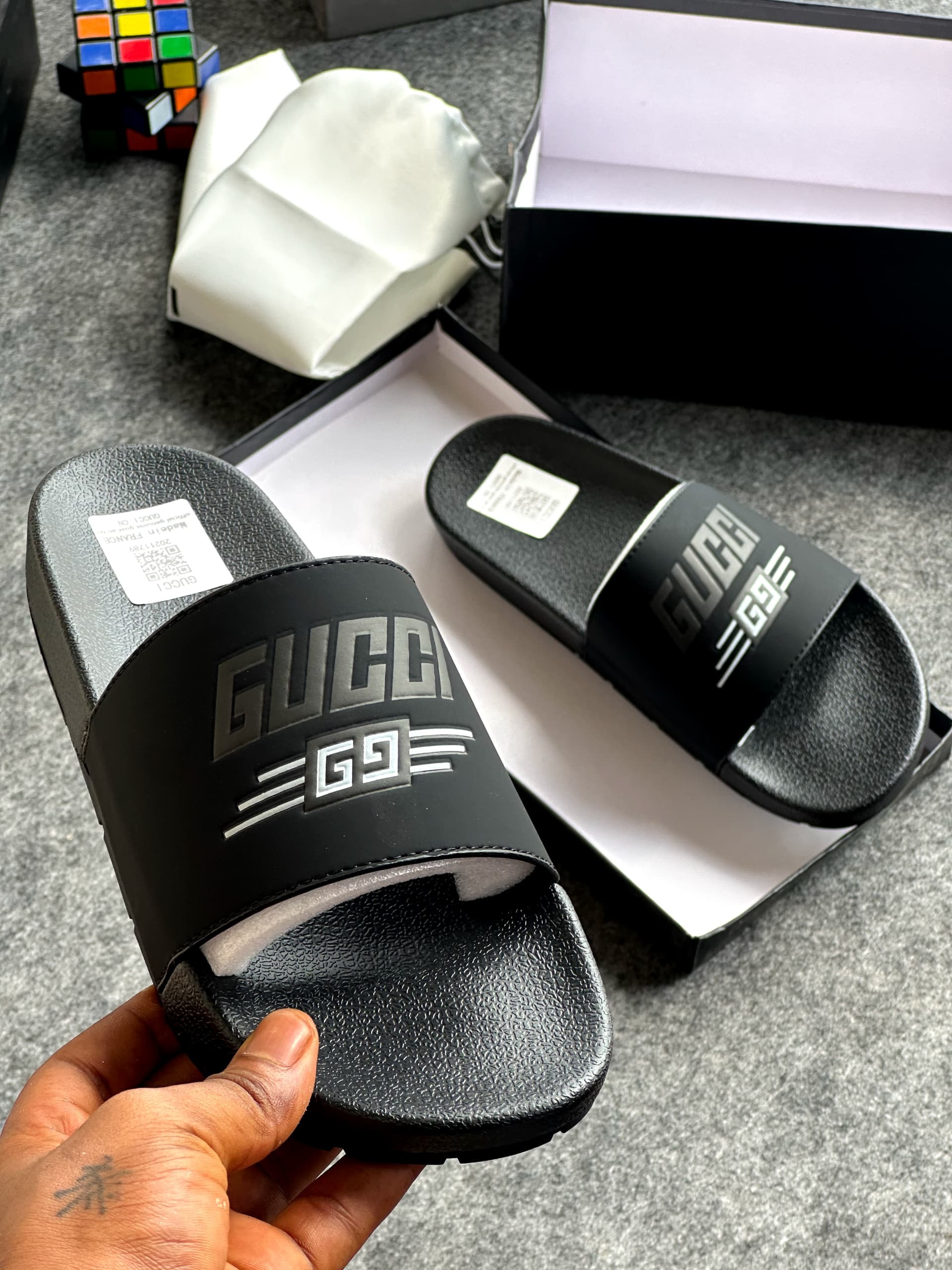 Black Gucci slides with raised GG logo held in front of branded packaging.