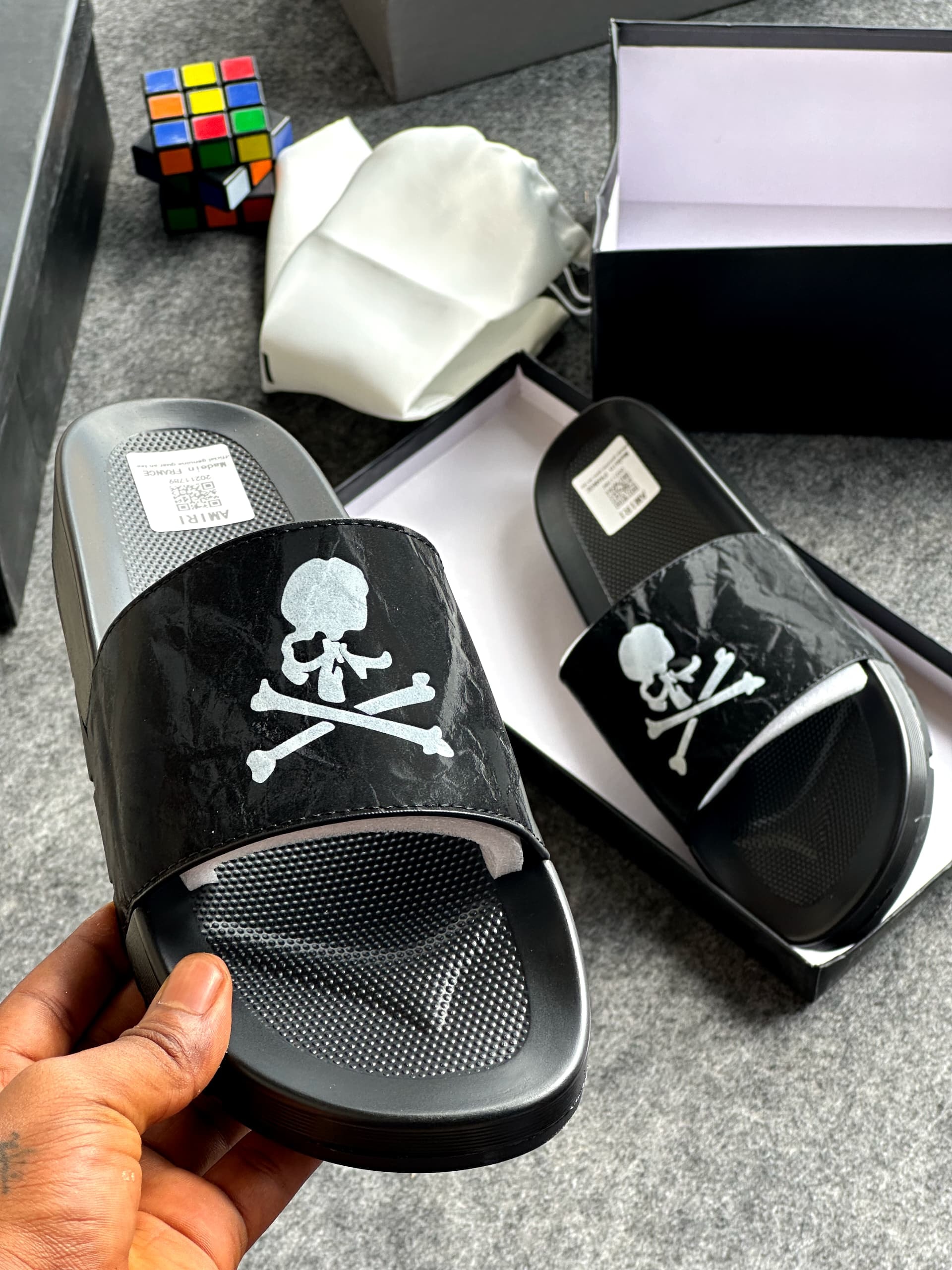 Black slides with silver skull and crossbones design displayed with box and accessories.