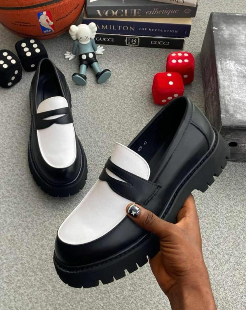 Black and white two-tone platform loafers with chunky soles, one held in hand showing the profile view.