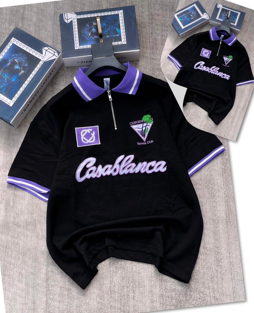 Black zip polo shirt with Casablanca graphics and purple trim on gray surface.