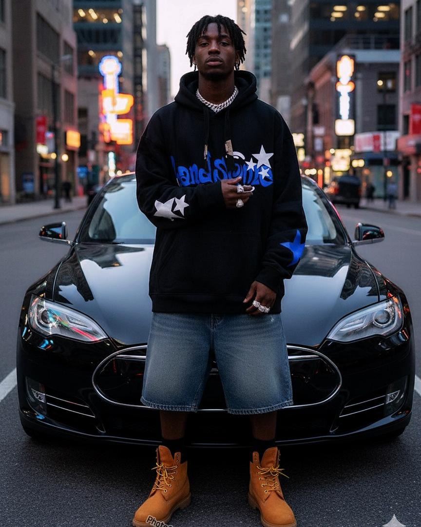 Man in black star graphic hoodie with blue text, standing in front of black car at night.