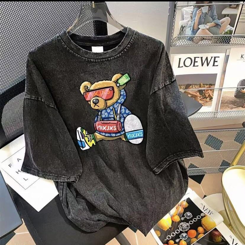 Dark washed t-shirt with colorful teddy bear graphic, hanging on a clear hanger.