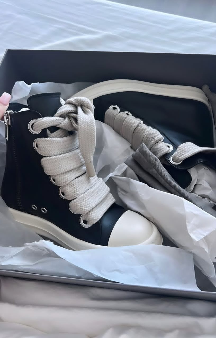 Black Rick Owens high-top sneakers with Jumbo Lace detail shown inside a box with tissue paper, highlighting the zipper and lacing system.