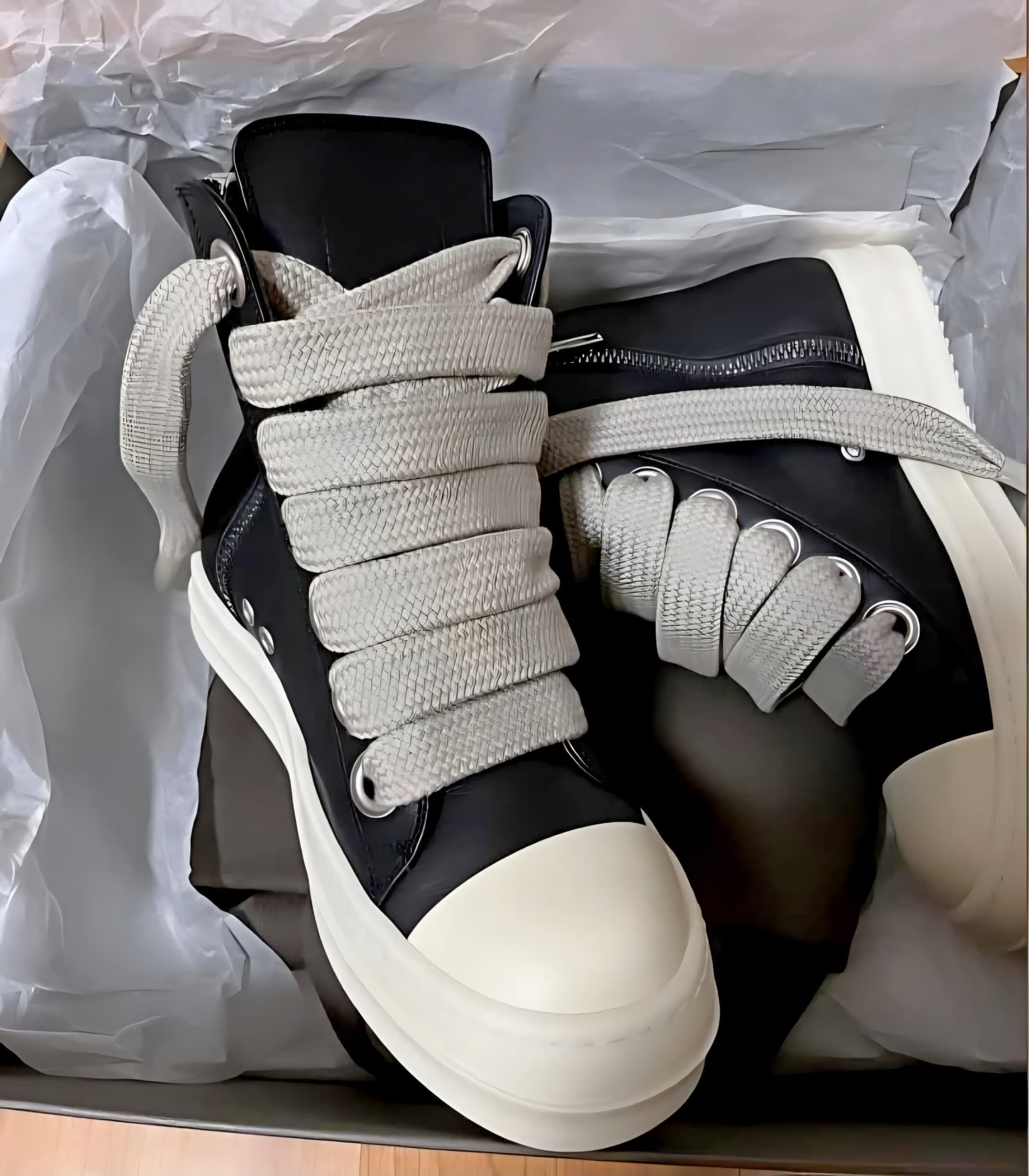Black Rick Owens high-top Jumbo Lace sneakers with white oversized laces and chunky sole, displayed on crumpled white paper.