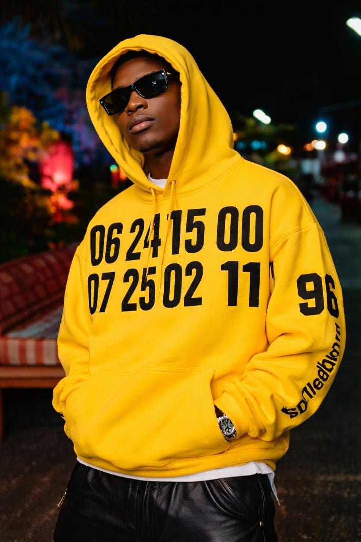 Man modeling yellow oversized graphic hoodie with numeric print at night.