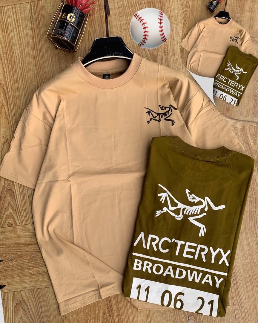 Beige and olive Arc'teryx graphic t-shirts on wooden background.