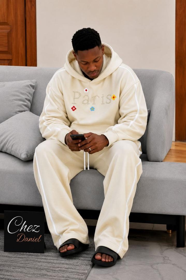 Model wearing cream Paris beaded two-piece hoodie and pants set with white piping.