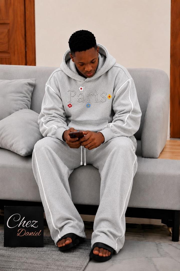Model wearing light gray Paris beaded two-piece hoodie and pants set with white piping.