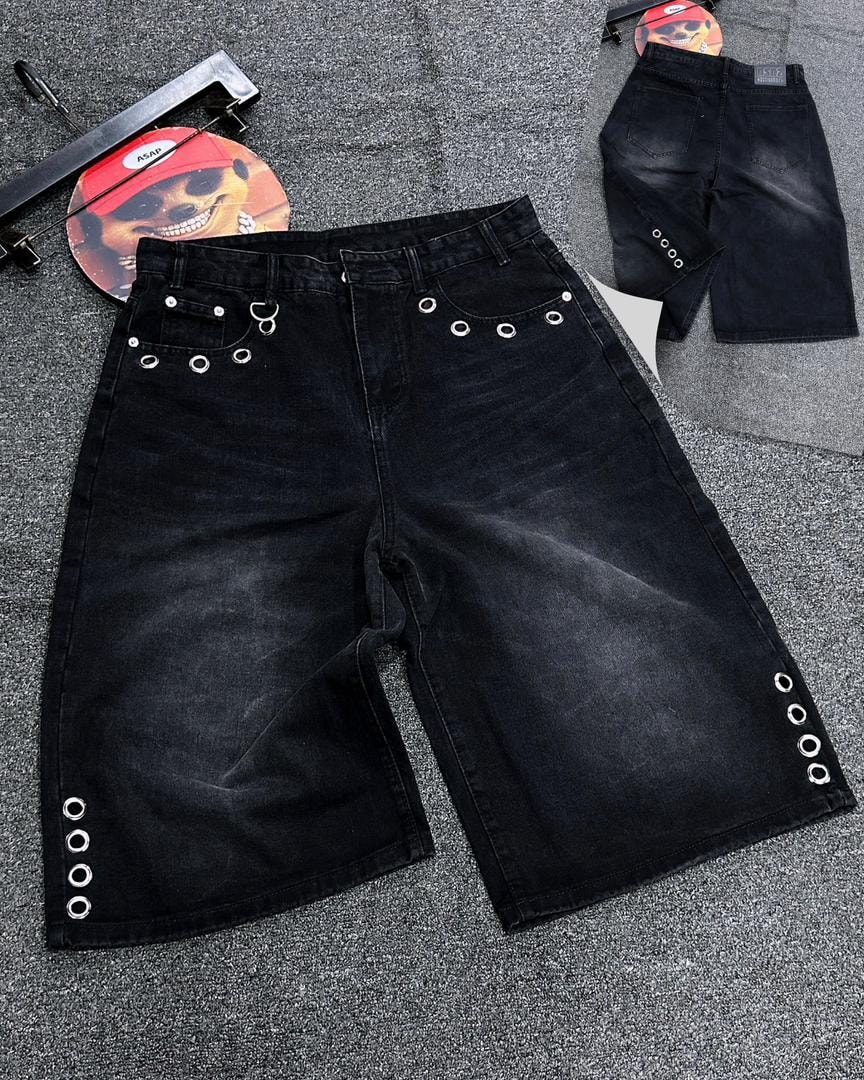 Black baggy denim jorts with silver grommets and rings, shown in front and back views on textured surface.