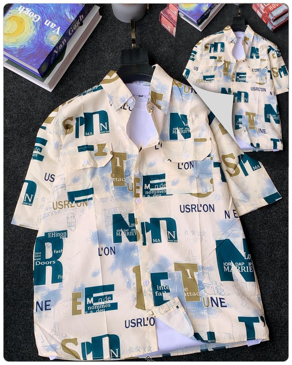 Cream short sleeve collared shirt with teal gold and brown text collage print beside Van Gogh book.