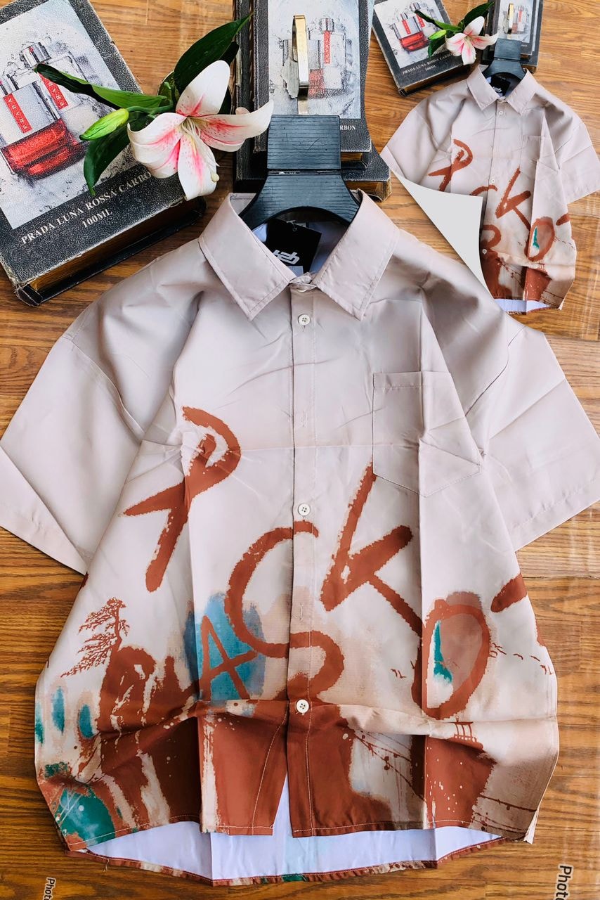 Beige short sleeve collared shirt with brown and teal calligraphy landscape print with books and lily.