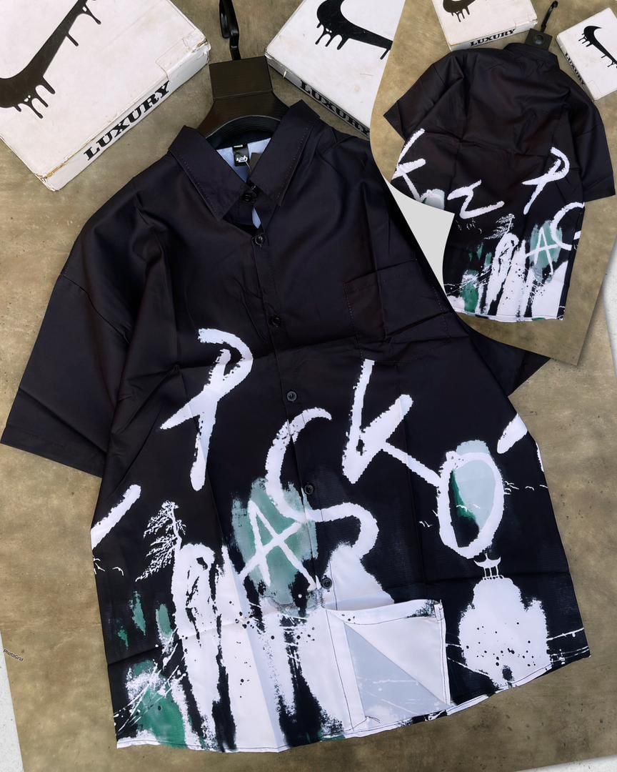 Black short sleeve button-down shirt with white and green landscape graffiti print beside luxury boxes.
