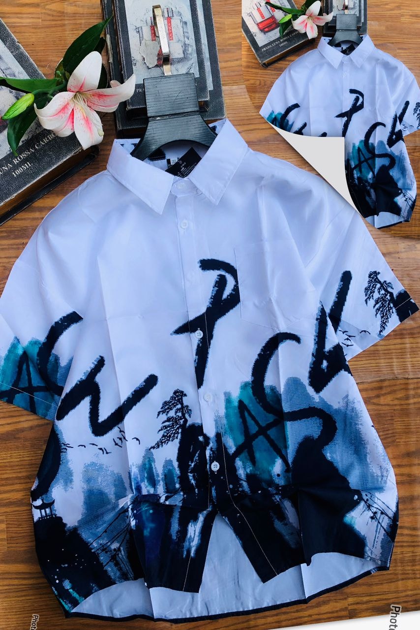 White short sleeve collared shirt with black and teal brushstroke landscape print on wooden surface with flowers.