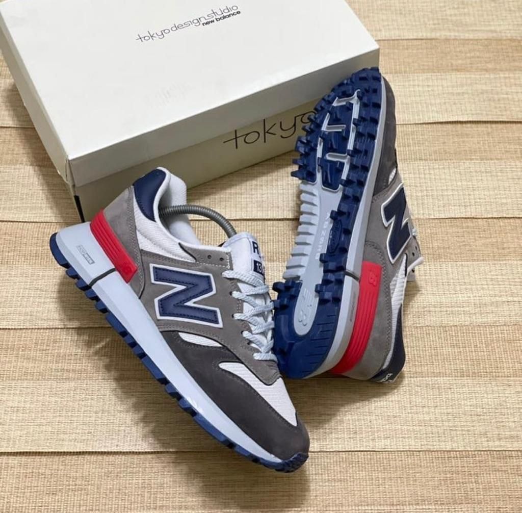 Grey, navy, white, and red New Balance 327 sneakers with white box on wooden surface.