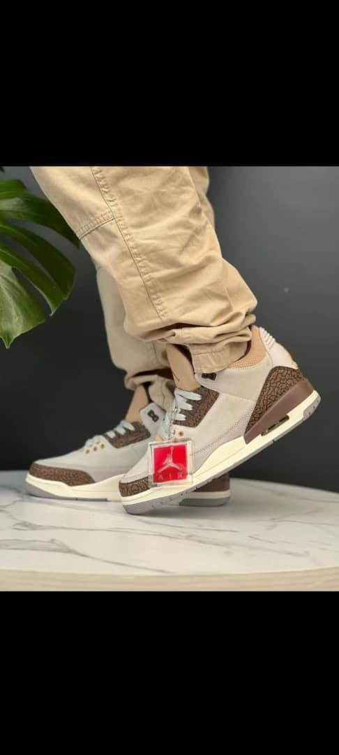 Air Jordan 3 Retro in beige brown and gray worn with beige pants on marble surface.