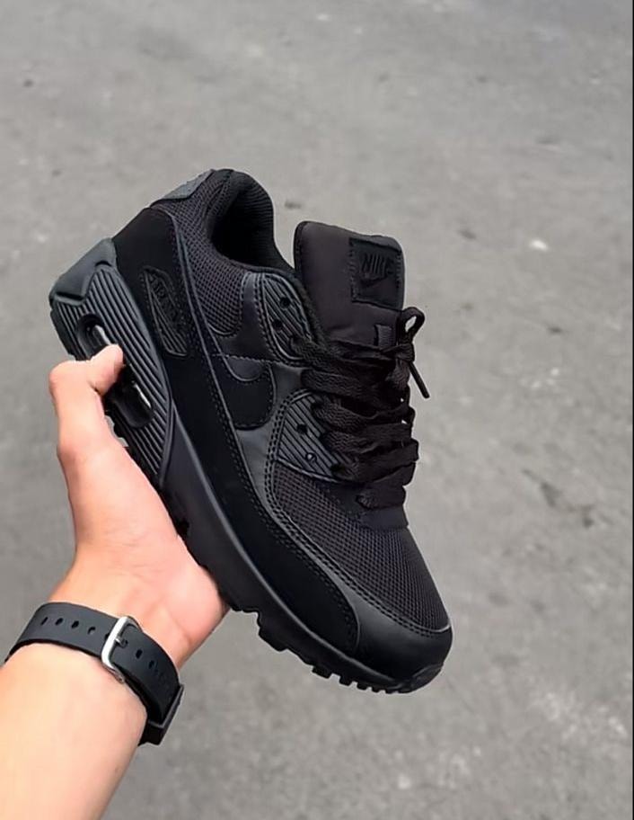 Black Nike Air Max sneakers held by hand outdoors showing side profile and air unit.