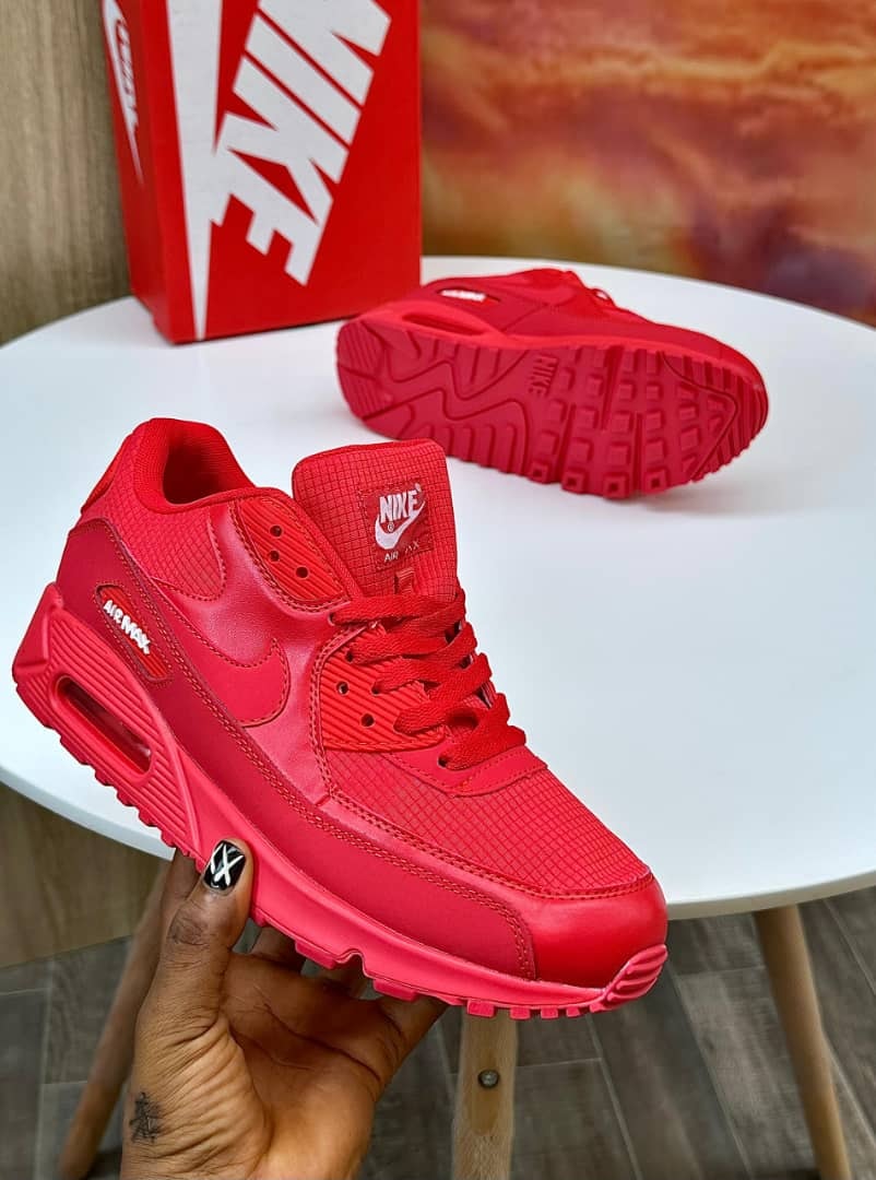 Nike Air Max sneakers in all red held by hand and shown from back on white table with red Nike box.