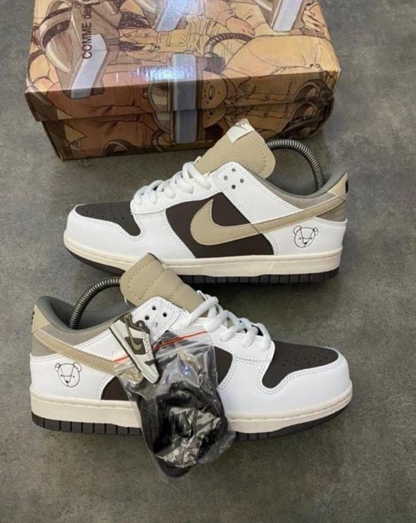Nike Dunk Low sneakers in white with brown panels, beige swoosh and bear logo detail.