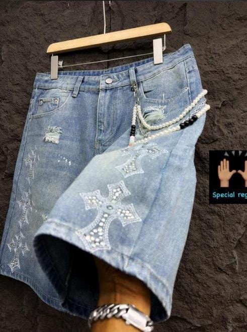 Person wearing light blue denim jorts with white cross designs, rips, and attached beaded chain.