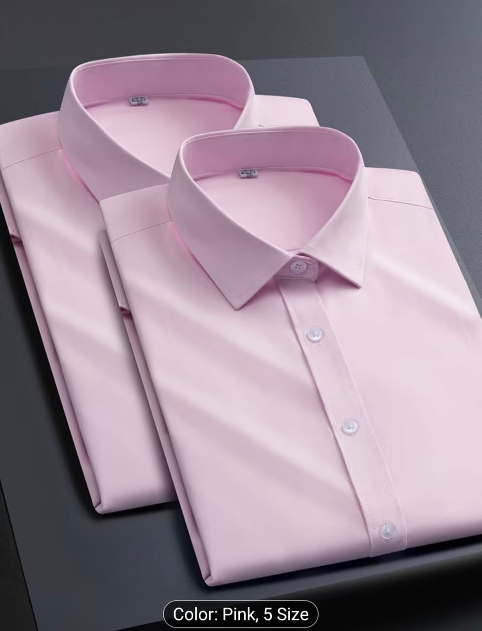 Pink long sleeve dress shirt folded on dark surface.