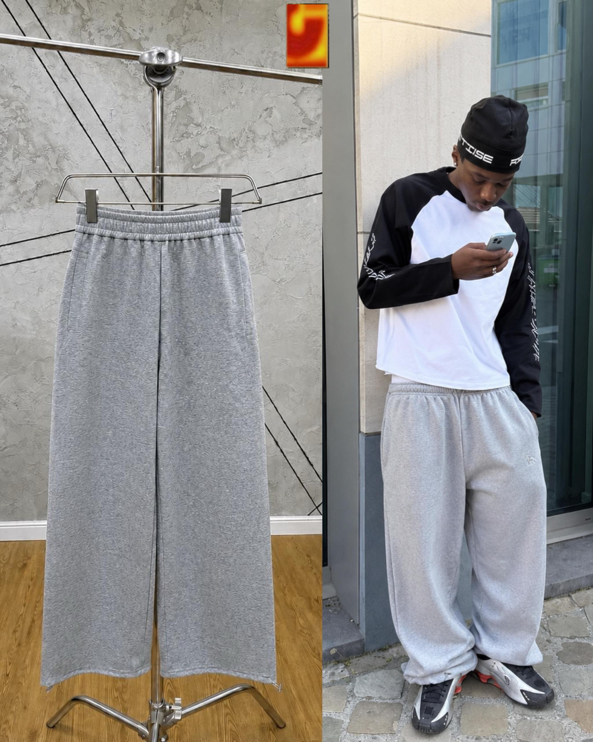Gray wide-leg joggers on metal hanger and model checking phone in urban setting.