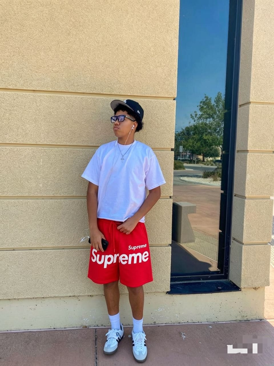Model wearing red Supreme logo fleece shorts with white tee, cap and sneakers.