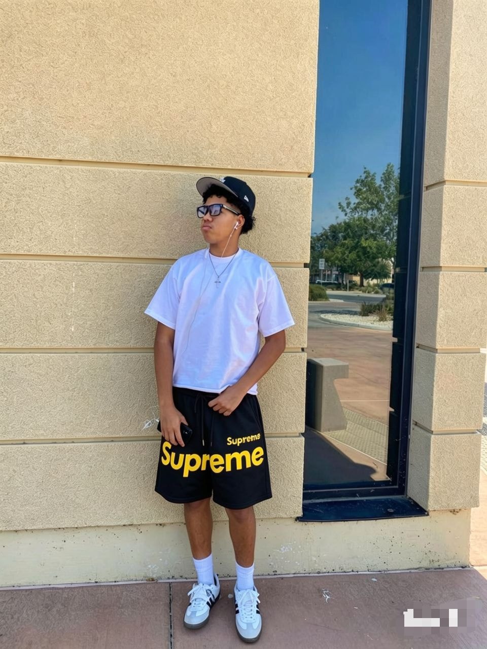 Model wearing black Supreme logo fleece shorts with white tee, cap and sneakers.