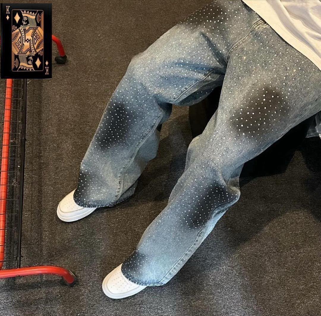 Model seated in gray baggy jeans with white dot patterns and faded areas, shown with white sneakers.