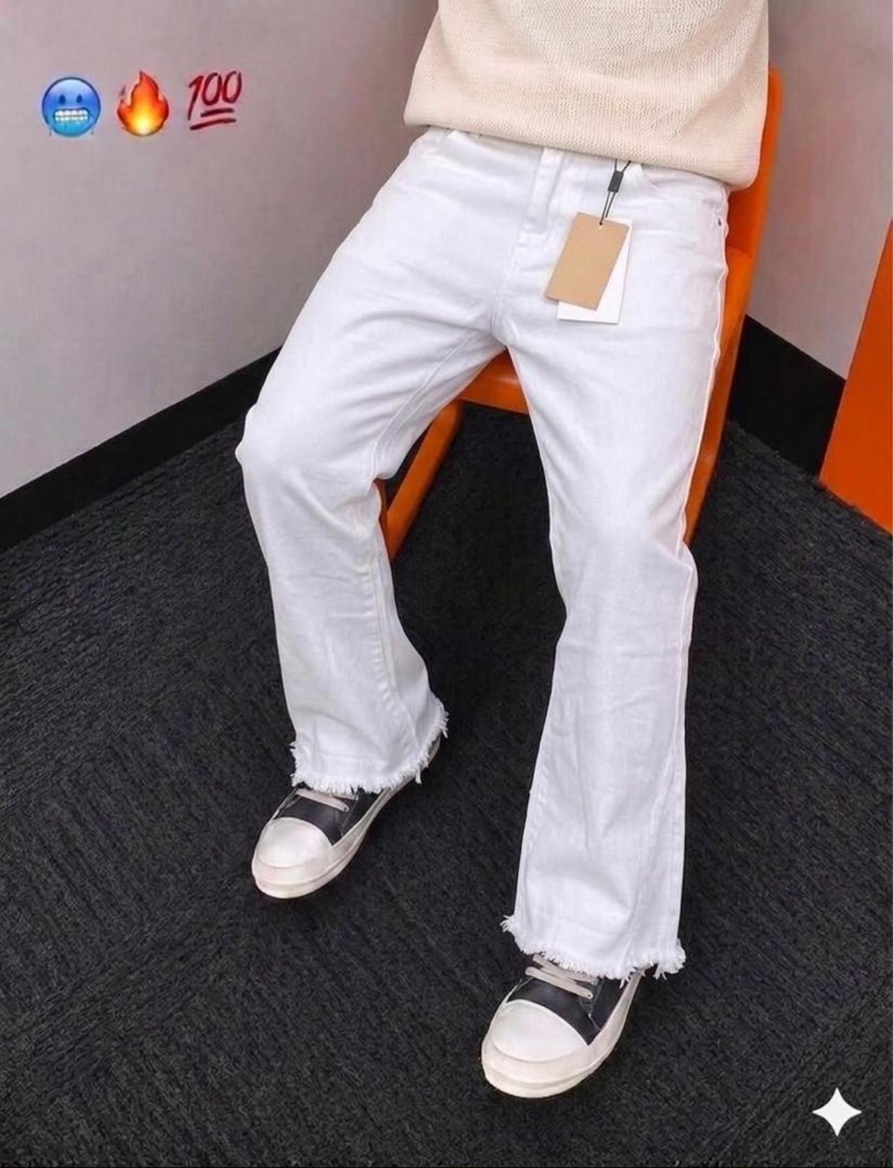 Model wearing white baggy jeans with frayed hems, seated on orange chair with cream sweater.