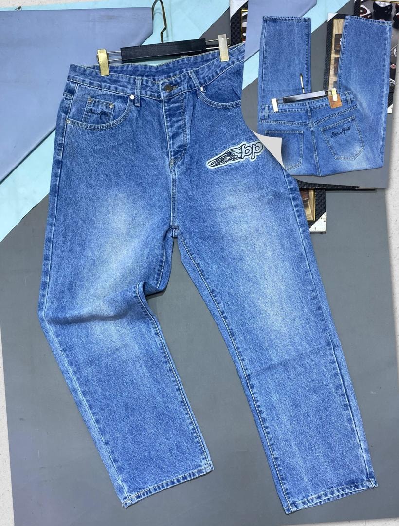 Blue baggy jeans with graphic logo on back pocket, flat lay with back view on gray surface.