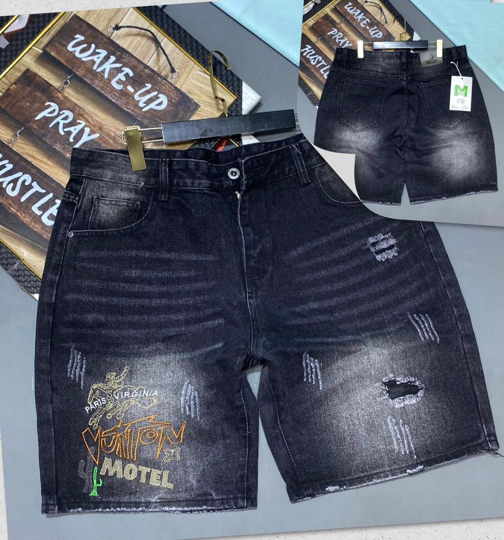 Front and back views of black graphic distressed denim jorts featuring VUITON MOTEL embroidery and tears.