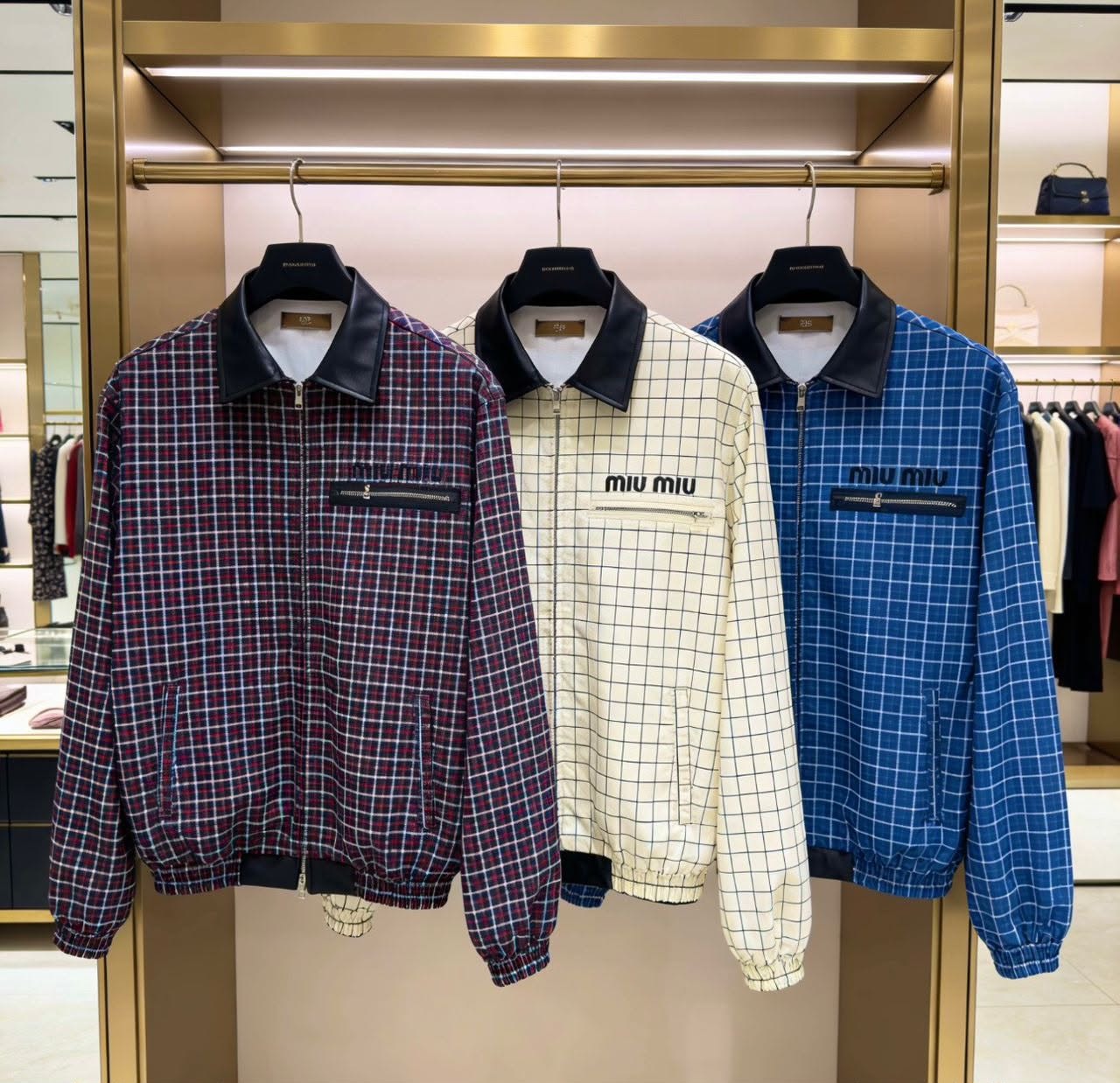 Three miu miu grid bomber jackets in red, cream, and blue hanging together in a store.