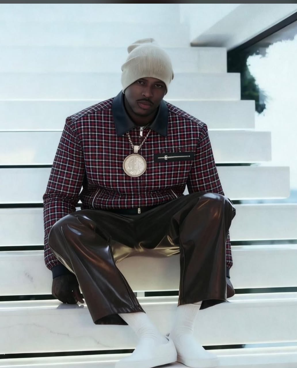 Model seated on stairs wearing red grid jacket with beige beanie and accessories.