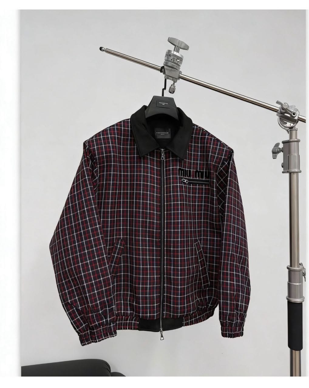 Red and black checkered bomber jacket hanging on a metal stand.