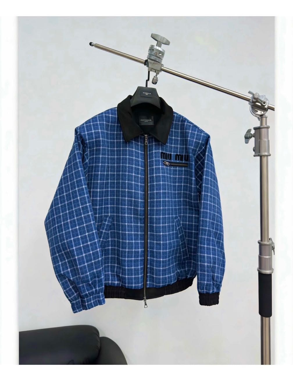 Blue grid print jacket hanging on a stand against white background.