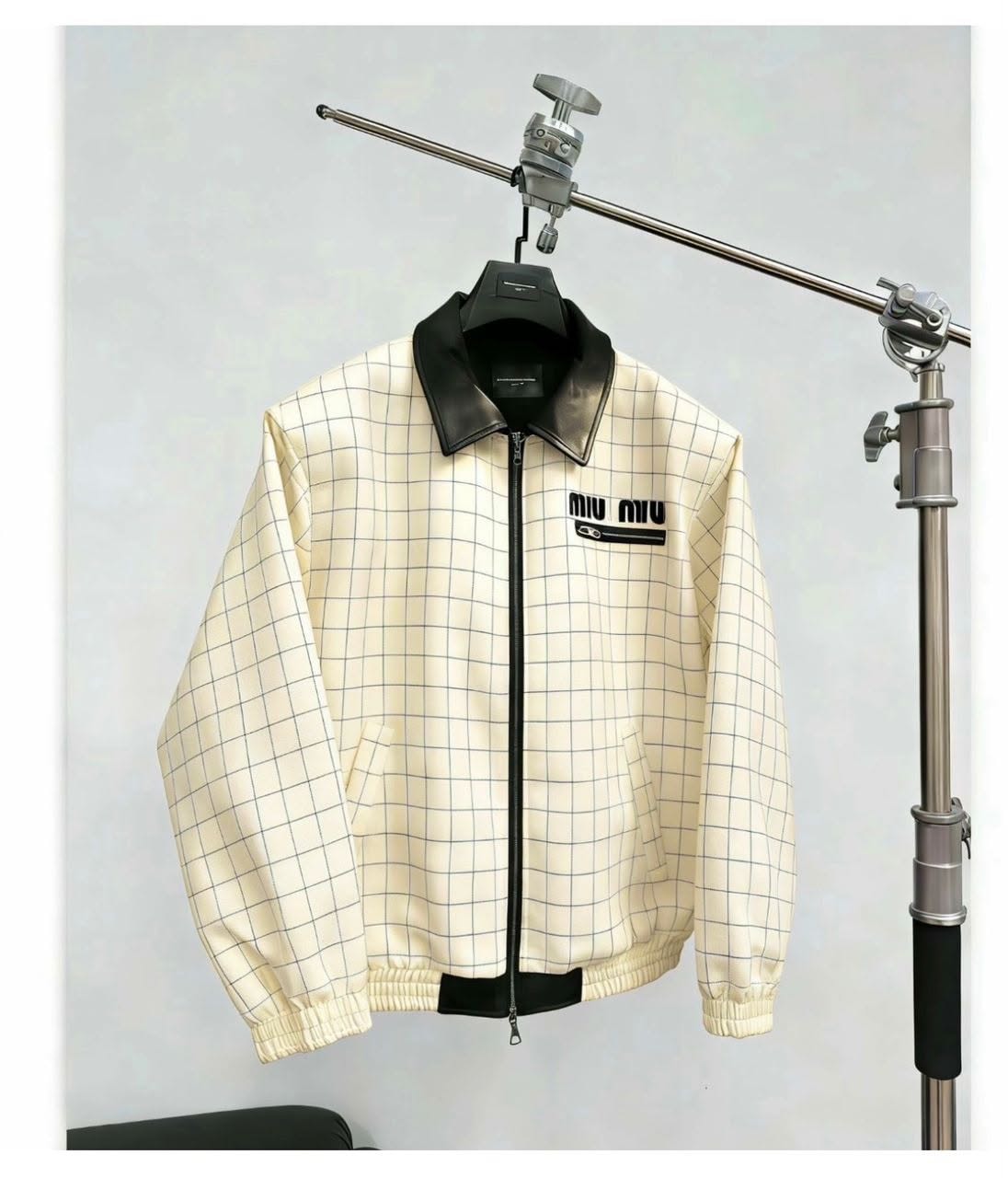Cream grid bomber jacket hanging on a metal stand.