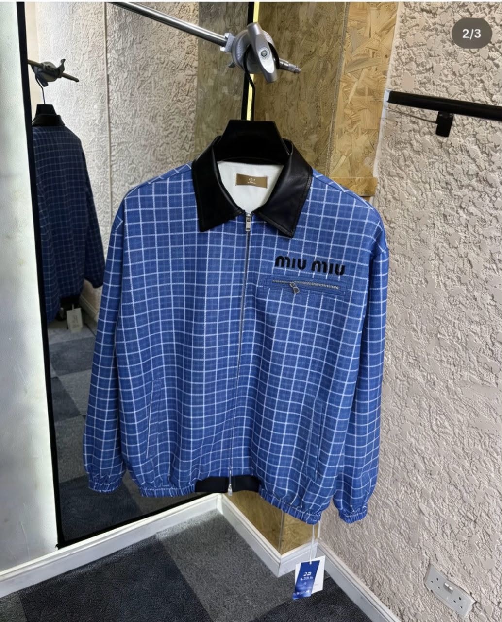 Blue grid print bomber jacket hanging in a showroom.